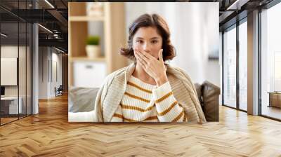 cold and health problem concept - sick woman in blanket coughing or covering mouth by hand at home Wall mural