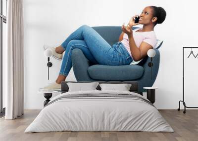 comfort, people and furniture concept - portrait of happy smiling young african american woman calling on smartphone sitting in modern armchair over white background Wall mural