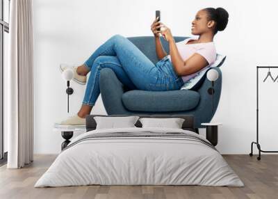 comfort, people and furniture concept - portrait of happy smiling young african american woman with smartphone sitting in modern armchair over white background Wall mural