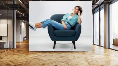 comfort, people and furniture concept - portrait of happy smiling young woman in turquoise shirt and jeans sitting in modern armchair over grey background Wall mural