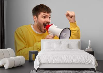 communication and people concept - angry young man in yellow sweatshirt shouting to megaphone over grey background Wall mural