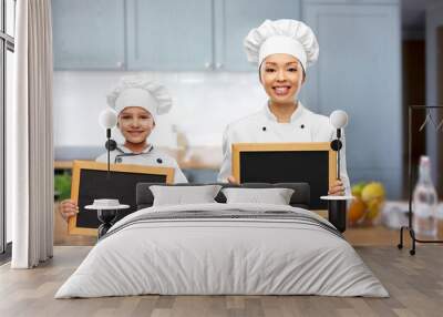 cooking, advertisement and people concept - happy smiling female chef and little girl holding black chalkboards over kitchen background Wall mural