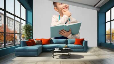 cooking, culinary and profession concept - happy smiling little boy in apron reading cook book and thinking over grey background Wall mural