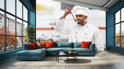 cooking, profession and people concept - happy male indian chef in toque tasting food from ladle over restaurant kitchen background Wall mural