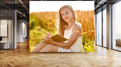 country, literature and leisure concept - smiling young girl in white dress writing to diary or drawing to sketchbook on cereal field in summer Wall mural