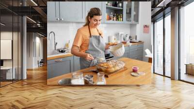 culinary, bake and cooking food concept - happy smiling young woman adding buttercream topping to baked roll buns in baking dish on kitchen at home Wall mural