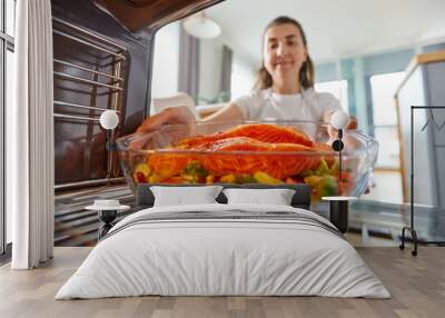 culinary, food and people concept - woman cooking salmon fish with vegetables in baking dish in oven at home kitchen Wall mural