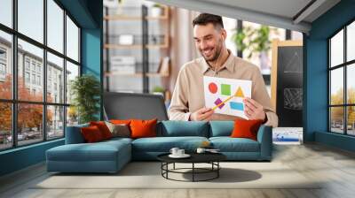 distance education, primary school and remote job concept - happy smiling male teacher with laptop and picture of geometric shapes in different colors having online class at home office Wall mural