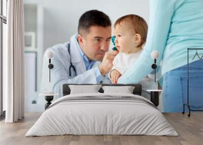 doctor checking baby ear with otoscope at clinic Wall mural