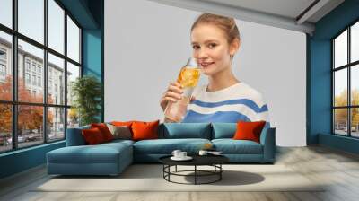 drink, health and people concept - happy smiling teenage girl in sweater with orange fruit infused water in glass bottle over grey background Wall mural