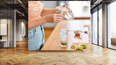 drinks and people concept - close up of woman pouring water from glass bottle to jigger and making lime mojito cocktail at home kitchen Wall mural