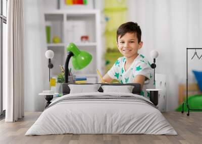 education, childhood and school concept - happy little boy sitting at desk and writing to notebook at home Wall mural