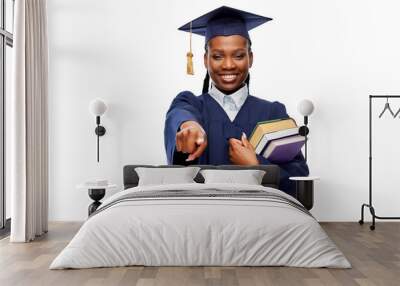 education, graduation and people concept - happy graduate student woman in mortarboard and bachelor gown with books pointing finger to camera over white background Wall mural