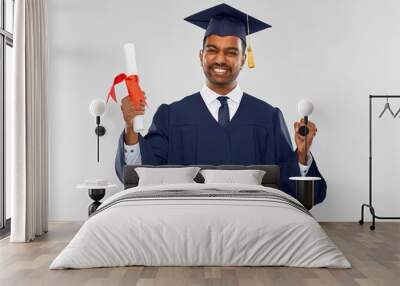 education, graduation and people concept - happy smiling indian male graduate student in mortar board and bachelor gown with diploma celebrating success over grey background Wall mural