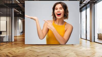 emotions and people concept - happy smiling young woman in mustard yellow top holding something on empty hand over grey background Wall mural