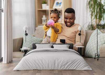 family, fatherhood and technology concept - african american father with smartphone and little baby daughter playing with ball at home Wall mural