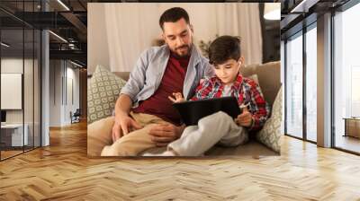 family, fatherhood and technology concept - happy father and little son with tablet pc computer and earphones listening to music at home Wall mural