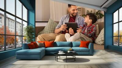 family, fatherhood and technology concept - happy father and little son with tablet pc computer and earphones listening to music at home Wall mural