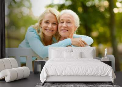 family, generation and people concept - happy smiling young daughter with senior mother sitting on park bench and hugging Wall mural