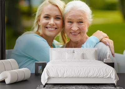 family, generation and people concept - happy smiling young daughter with senior mother sitting on park bench and hugging Wall mural