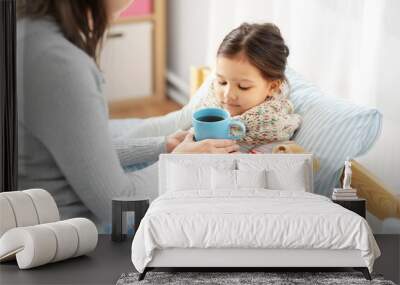 family, health and people concept - mother giving mug with hot tea to sick little daughter lying in bed at home Wall mural