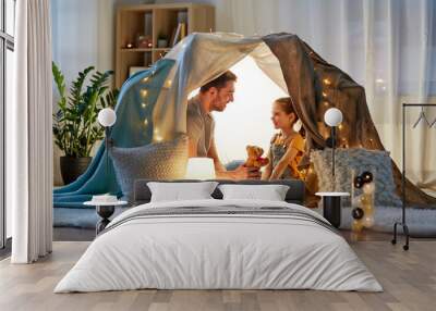 family, hygge and people concept - happy father with teddy bear toy and little daughter playing in kids tent at night at home Wall mural