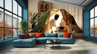 family, hygge and technology concept - happy mother and little daughter with tablet pc computer in kids tent at night at home Wall mural