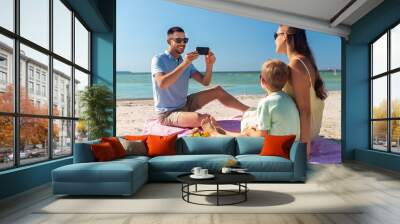 family, leisure and people concept - happy father with smartphone photographing mother and son on summer beach Wall mural