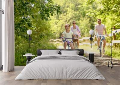 family, leisure and people concept - happy mother, father and little daughter riding bicycles in summer park Wall mural