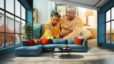 family, parenthood and people concept - happy african american father and baby daughter playing with toy blocks at home Wall mural