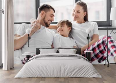 family, rest and people concept - happy mother, father and little son in matching pajamas sitting in bed in morning Wall mural