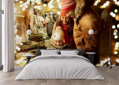 family, winter holidays and celebration concept - happy mother, father and little daughter buing wreath at christmas market on town hall square in tallinn, estonia Wall mural