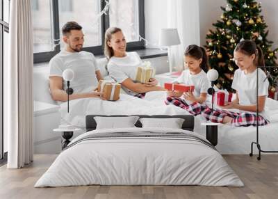 family, winter holidays and people concept - happy mother, father and two daughters in pajamas with christmas gifts in bed at home Wall mural