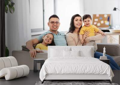 family and people concept - portrait of happy mother, father, little daughter and baby son sitting on sofa at home Wall mural