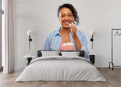 fast food and people concept - happy african american young woman eating popcorn from striped bucket over grey background Wall mural