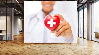 female doctor holding heart with red cross symbol Wall mural