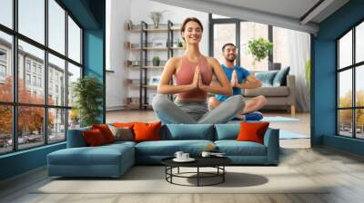 fitness, people and healthy lifestyle concept - happy smiling man and woman meditating in yoga lotus pose at home Wall mural