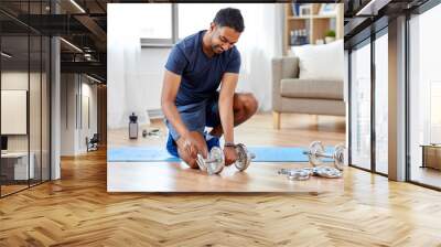 fitness, sport, weightlifting and bodybuilding concept - smiling indian man assembling dumbbells at home Wall mural