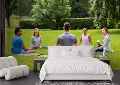 fitness, sport and healthy lifestyle concept - group of happy people sitting on yoga mats at park Wall mural