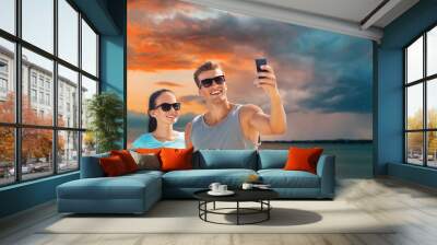 fitness, sport and healthy lifestyle concept - happy couple in sports clothes and sunglasses taking selfie by smartphone over sea and sunset sky background Wall mural