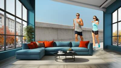 fitness, sport and lifestyle concept - happy couple in sports clothes and sunglasses running outdoors Wall mural