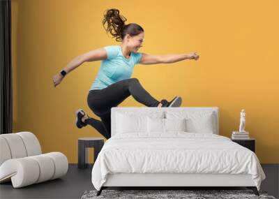 fitness, sport and people concept - happy smiling young woman jumping in air over yellow background Wall mural