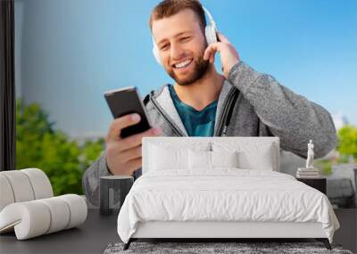 fitness, sport and technology concept - happy smiling young man with headphones and smartphone listening to music outdoors Wall mural