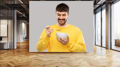 food and people concept - happy smiling young man eating cereals over grey background Wall mural