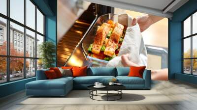 food cooking, culinary and people concept - young woman with towel taking baking dish with salmon fish and vegetables out of oven at home kitchen Wall mural