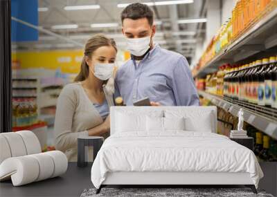 food shopping, consumerism and pandemic concept - happy couple wearing face protective medical masks for protection from virus disease with smartphone buying olive oil at grocery store or supermarket Wall mural