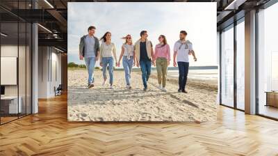 friendship, leisure and people concept - group of happy friends walking along beach in summer Wall mural