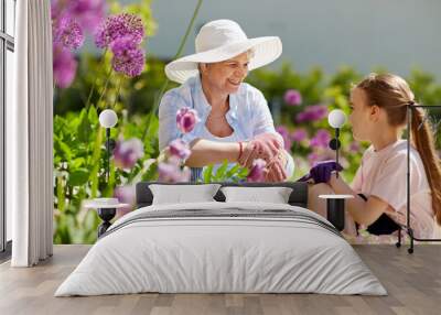 gardening, family and people concept - happy grandmother and granddaughter with flowers at summer garden Wall mural