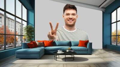 gesture and people concept - happy smiling young man in striped t-shirt showing peace hand sign over grey background Wall mural