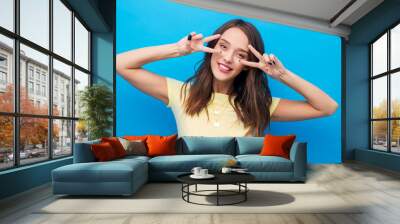 gesture and people concept - smiling young woman or teenage girl showing peace hand sign over bright blue background Wall mural